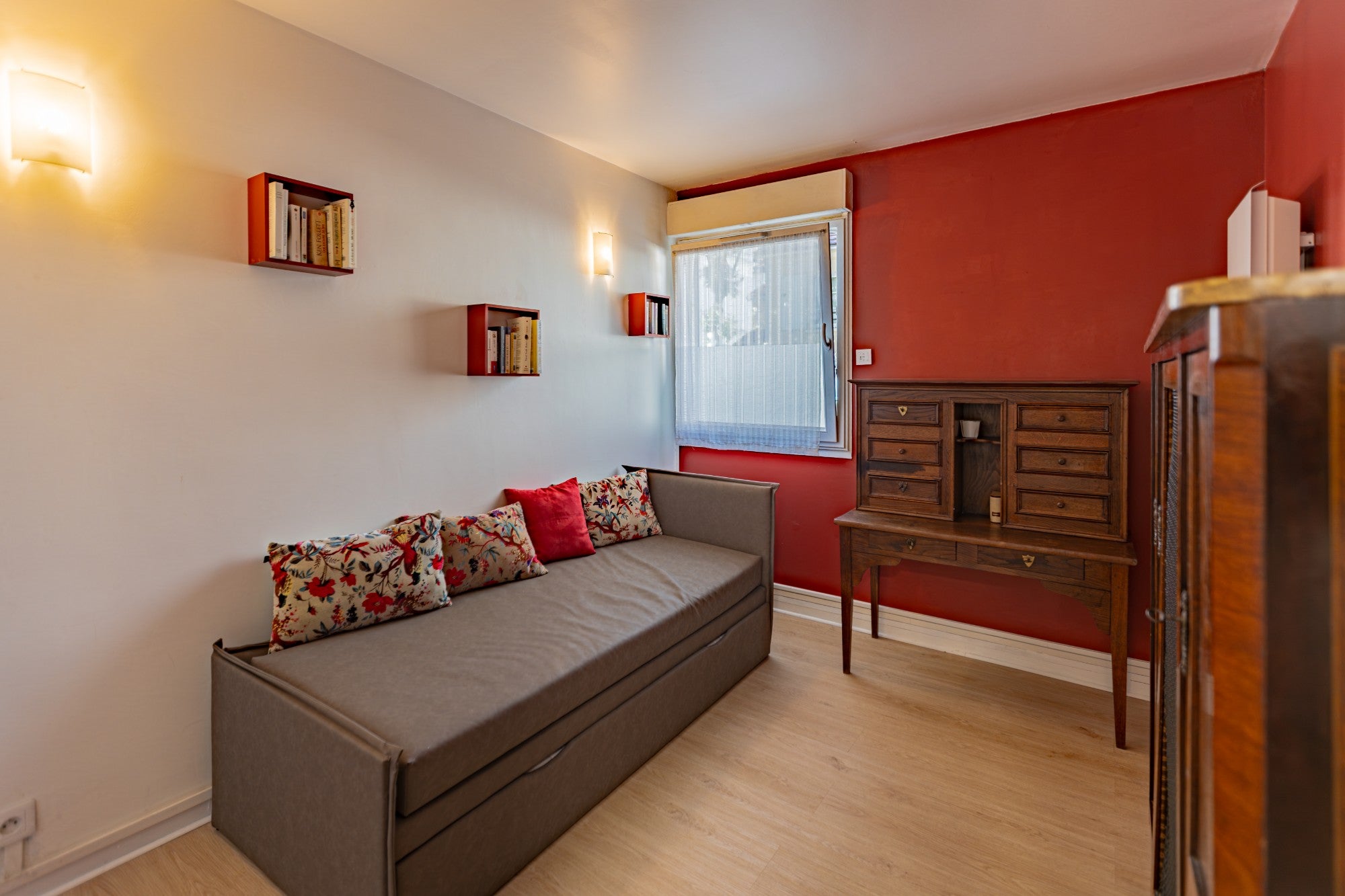 Pièce modulable avec banquette-lit, secrétaire ancien et mur rouge, photographiée par KEY STUDIO